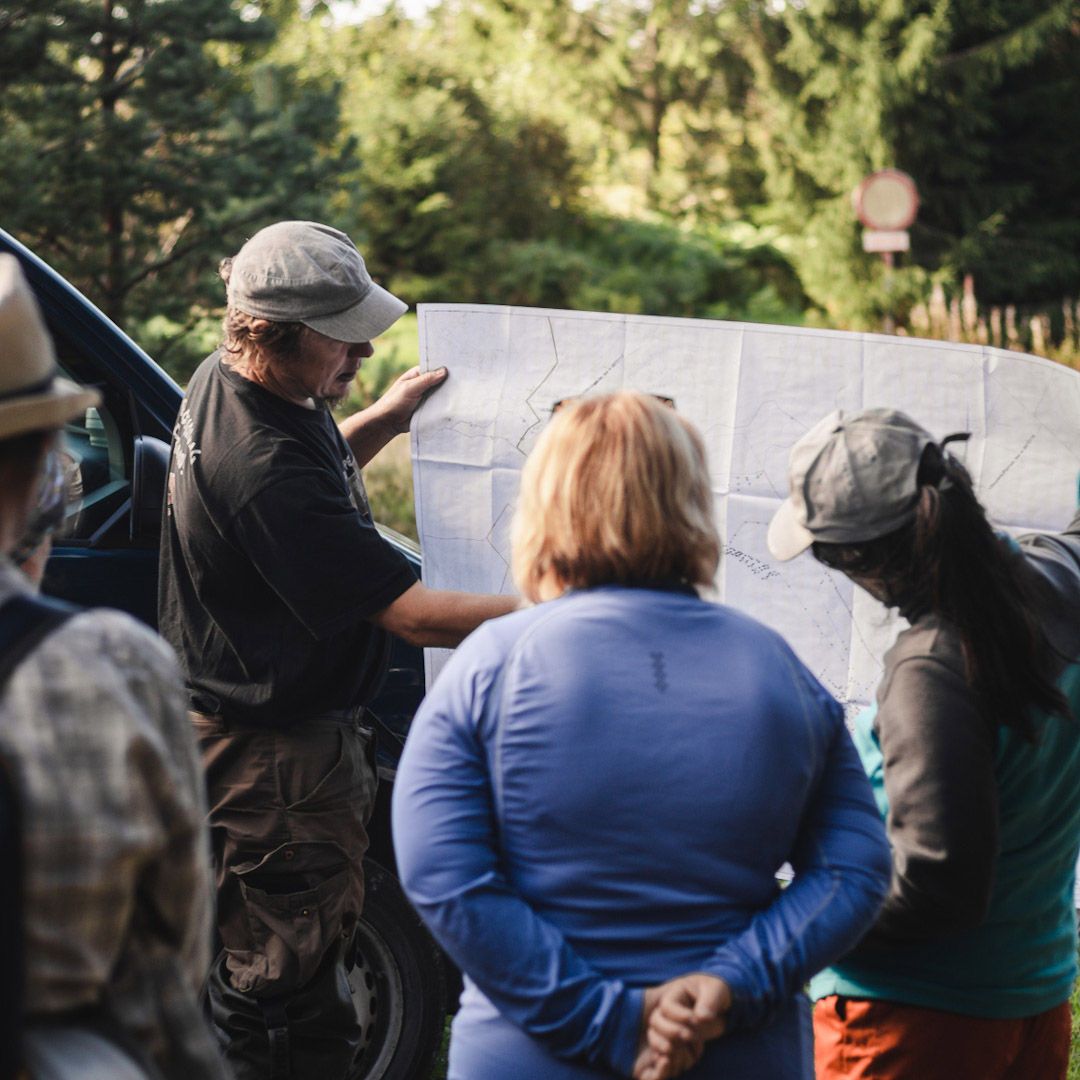 A group of people look at a map outdoors beside a vehicle.